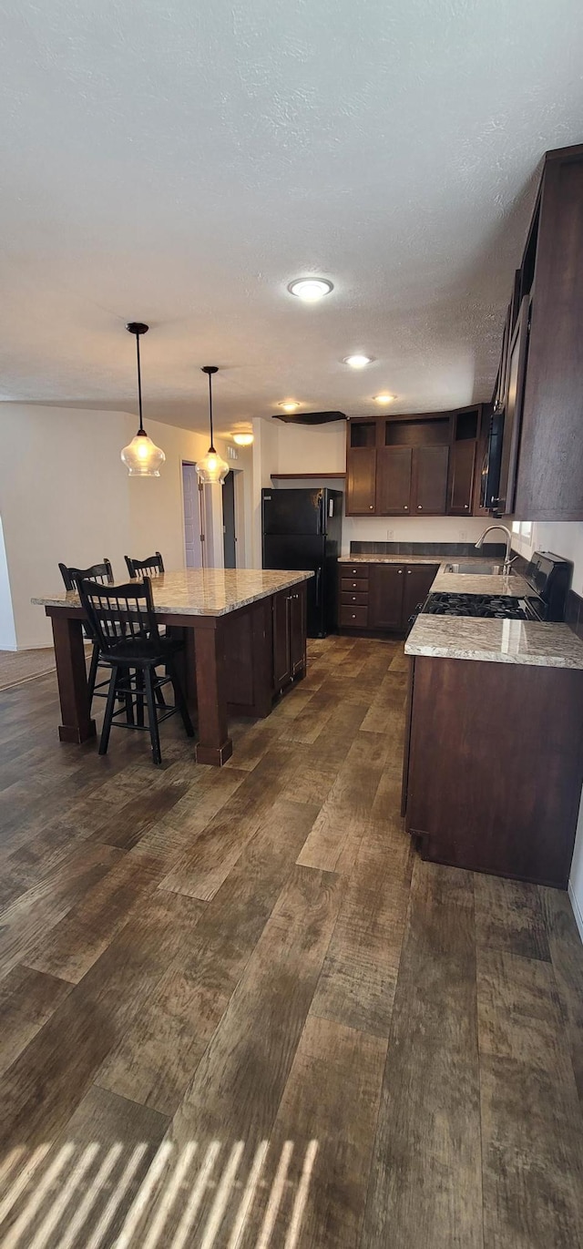 kitchen with light stone counters, freestanding refrigerator, a center island, and dark brown cabinetry