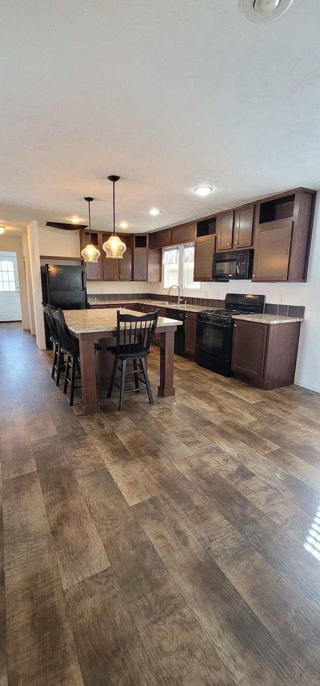 kitchen featuring a breakfast bar, hanging light fixtures, light countertops, a center island, and black appliances