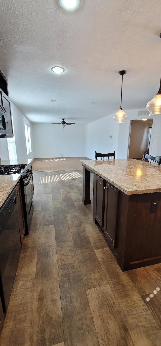 kitchen with visible vents, light stone counters, hanging light fixtures, dark brown cabinets, and black appliances