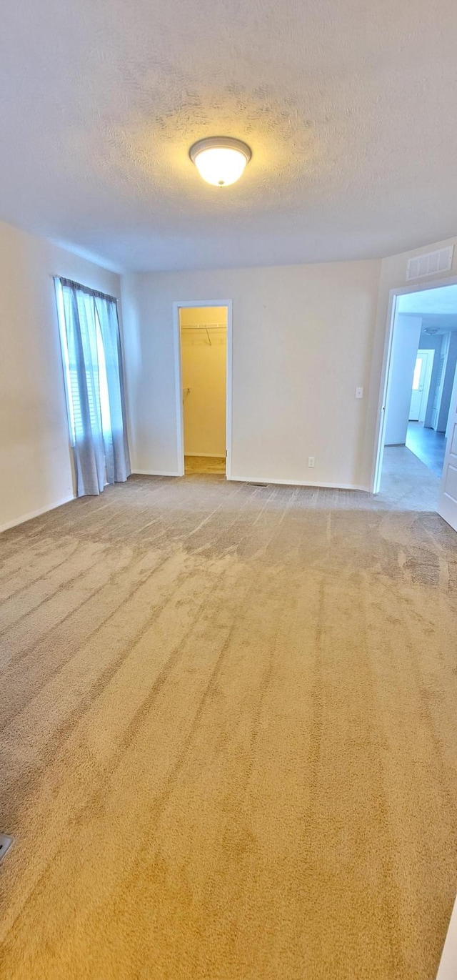 spare room with visible vents, a textured ceiling, and light colored carpet