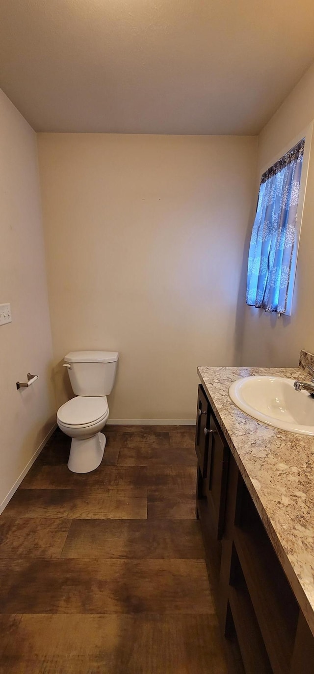 half bath featuring toilet, baseboards, wood finished floors, and vanity