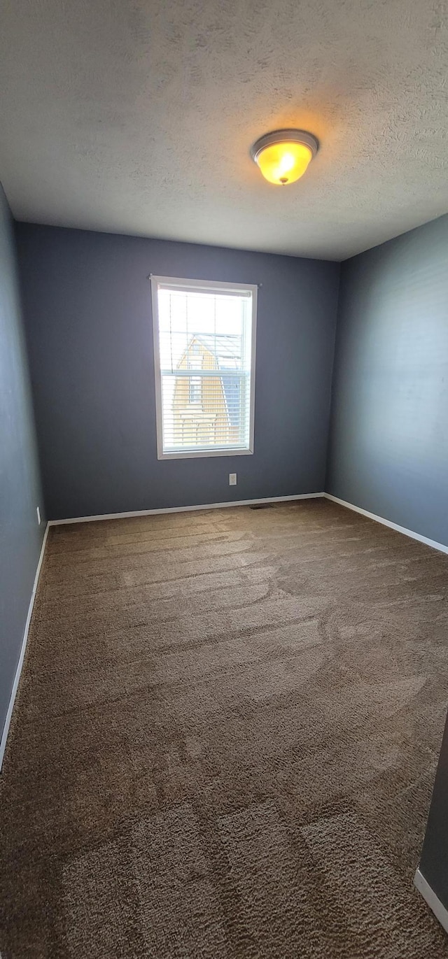 carpeted spare room with a textured ceiling and baseboards