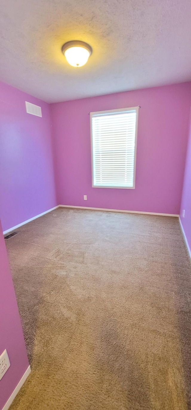 empty room featuring a textured ceiling, carpet flooring, visible vents, and baseboards