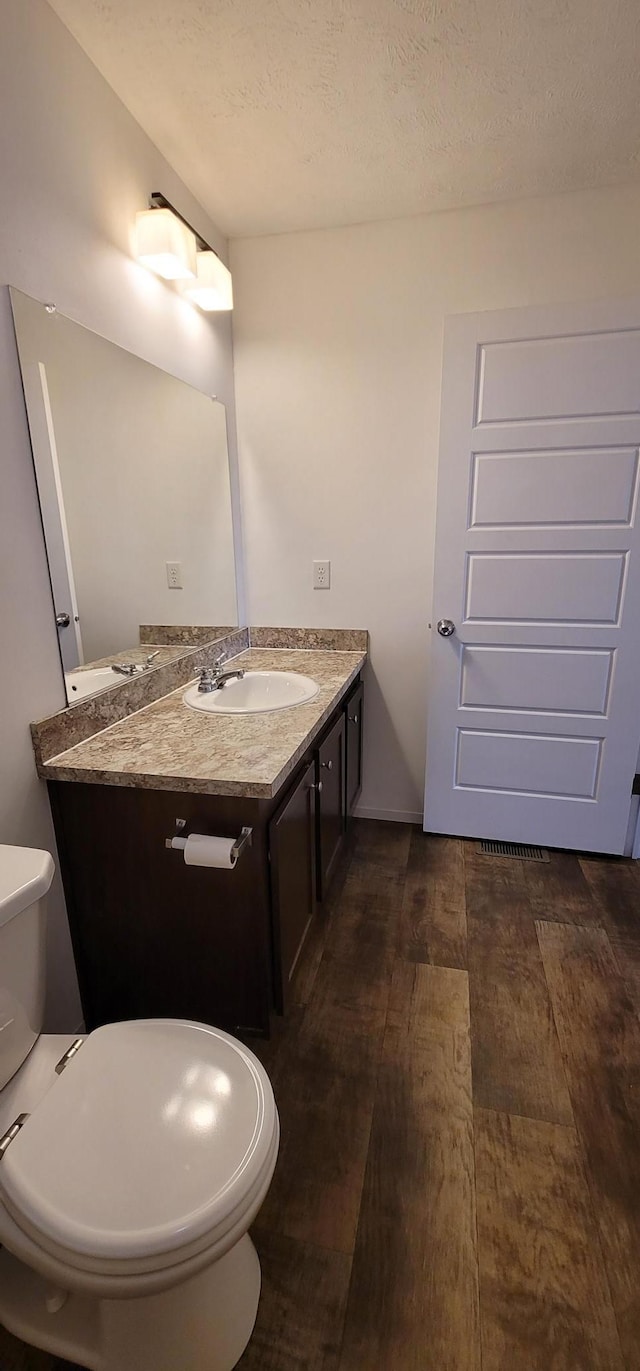 half bathroom with a textured ceiling, vanity, toilet, and wood finished floors