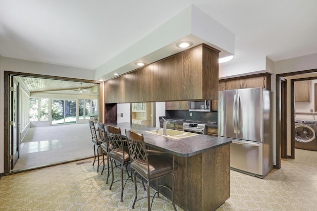 kitchen featuring sink, kitchen peninsula, washer / clothes dryer, stainless steel appliances, and a kitchen bar