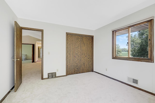 unfurnished bedroom featuring vaulted ceiling, a closet, and light colored carpet