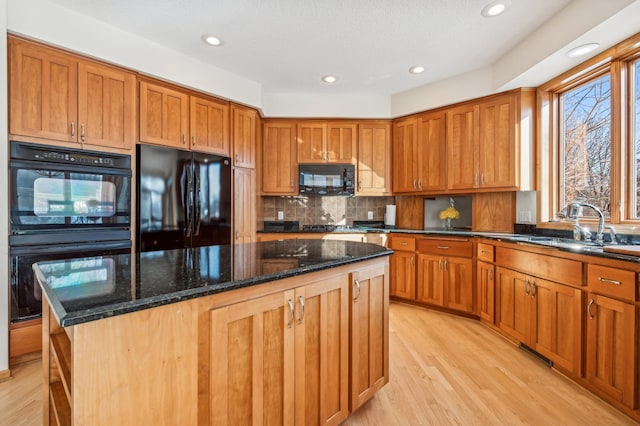 kitchen featuring sink, a center island, dark stone countertops, light wood-type flooring, and black appliances