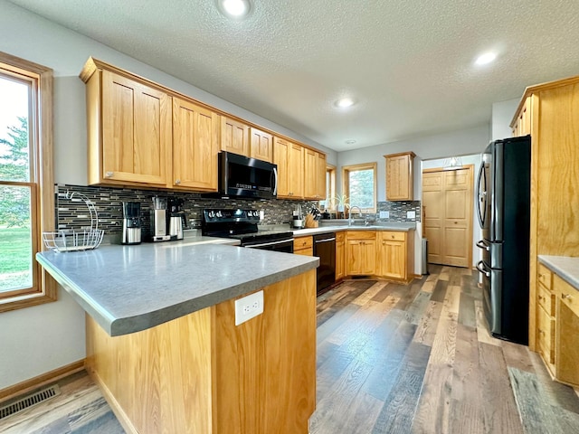 kitchen with kitchen peninsula, plenty of natural light, black appliances, and light hardwood / wood-style flooring