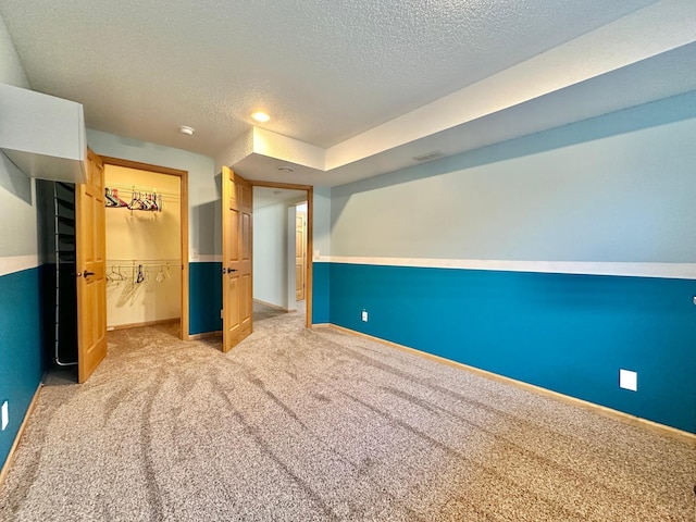 unfurnished bedroom featuring a spacious closet, a closet, light colored carpet, and a textured ceiling