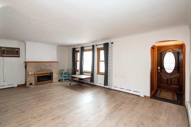 unfurnished living room with a wall mounted air conditioner, a healthy amount of sunlight, a fireplace, and light hardwood / wood-style flooring