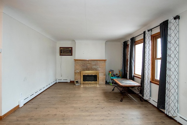 living area with a wall mounted air conditioner, light hardwood / wood-style flooring, baseboard heating, and a stone fireplace