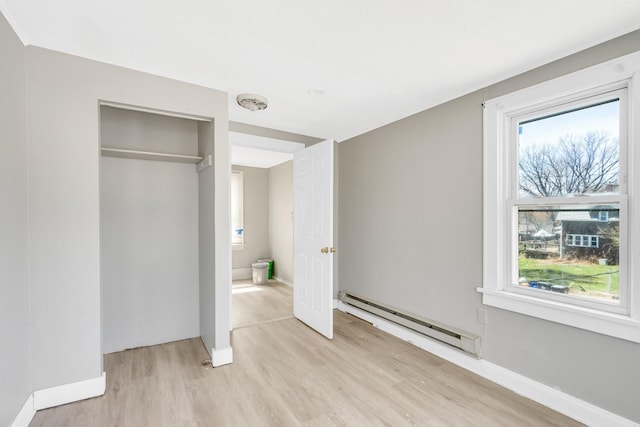 unfurnished bedroom with a baseboard heating unit, a closet, and light hardwood / wood-style flooring