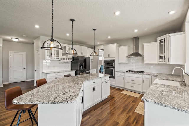 kitchen featuring white cabinetry, stainless steel appliances, a center island, sink, and wall chimney range hood