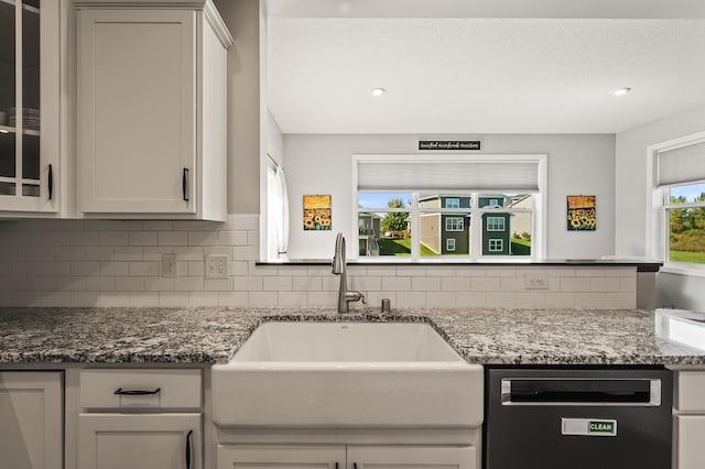 kitchen with sink, tasteful backsplash, stone counters, white cabinetry, and black dishwasher