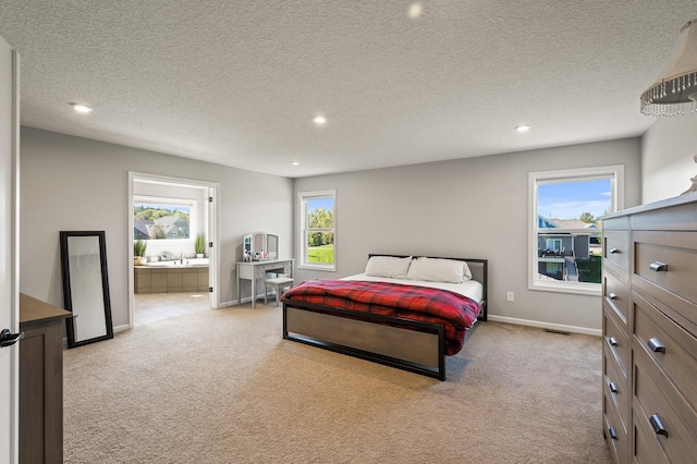 bedroom with a textured ceiling, ensuite bath, and light colored carpet