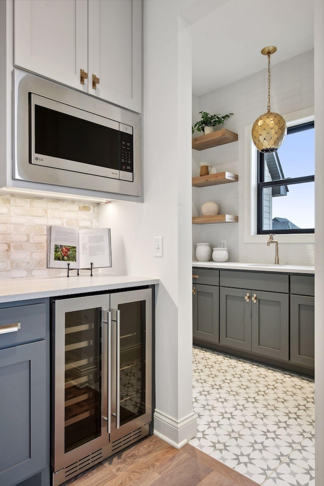 bar with light hardwood / wood-style floors, stainless steel microwave, pendant lighting, gray cabinets, and beverage cooler