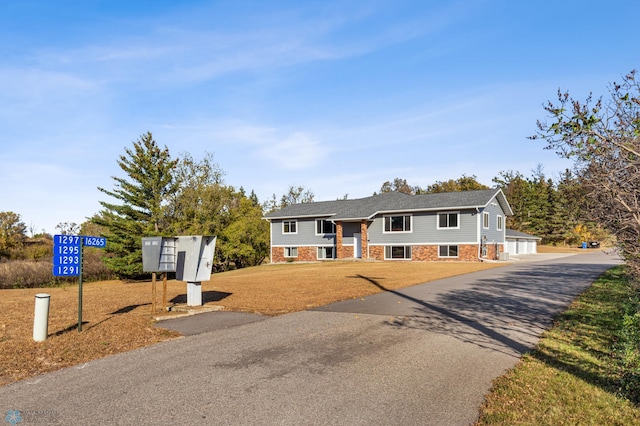 split foyer home featuring a front yard, brick siding, a garage, and aphalt driveway
