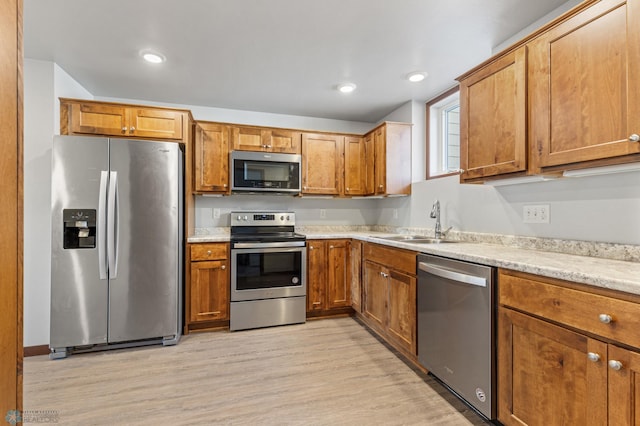 kitchen with light hardwood / wood-style flooring, stainless steel appliances, light stone countertops, and sink