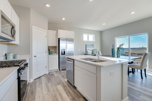 kitchen with a center island with sink, sink, light wood-type flooring, appliances with stainless steel finishes, and white cabinetry