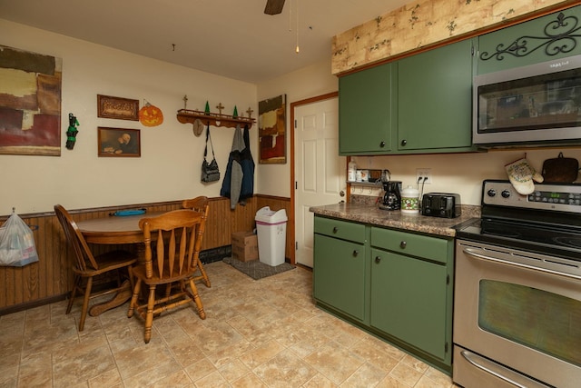 kitchen with wooden walls, green cabinetry, ceiling fan, and stainless steel appliances