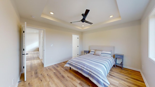 bedroom with light hardwood / wood-style flooring, ceiling fan, and a tray ceiling