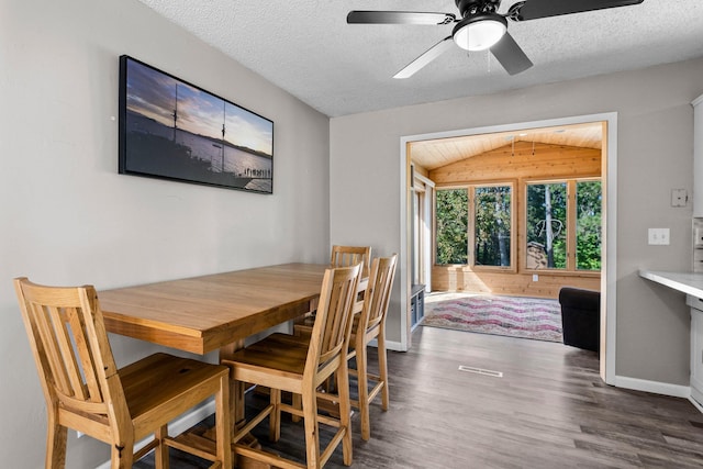 dining space with ceiling fan, lofted ceiling, a textured ceiling, wooden walls, and dark wood-type flooring