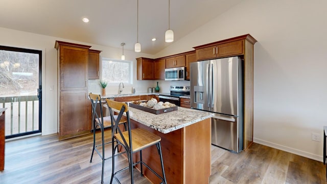 kitchen featuring sink, light stone counters, hanging light fixtures, appliances with stainless steel finishes, and a kitchen island