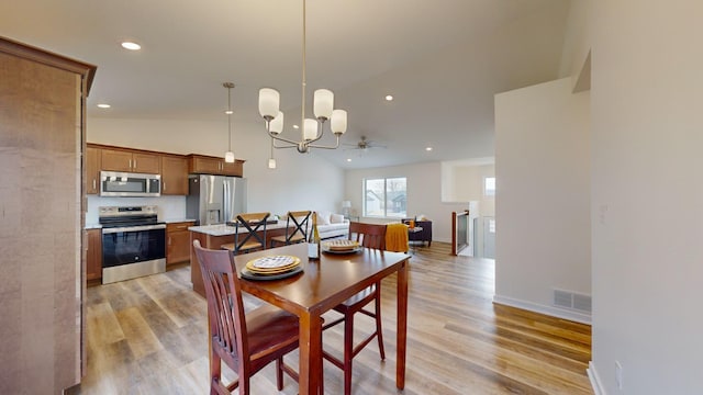 dining room featuring ceiling fan with notable chandelier, vaulted ceiling, and light hardwood / wood-style flooring