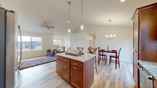 kitchen featuring hanging light fixtures, stainless steel appliances, light stone counters, a kitchen bar, and light wood-type flooring