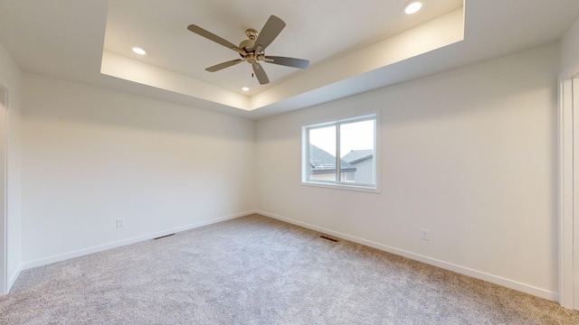 spare room with ceiling fan, light colored carpet, and a tray ceiling