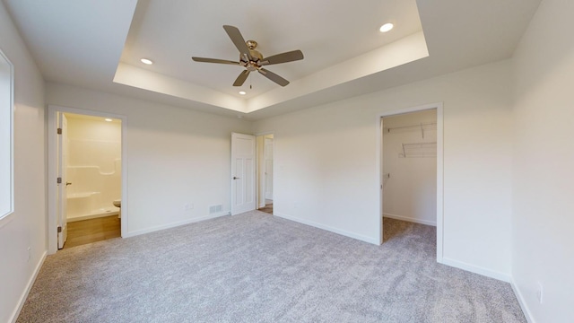 unfurnished bedroom with a tray ceiling, light colored carpet, ensuite bathroom, and a spacious closet