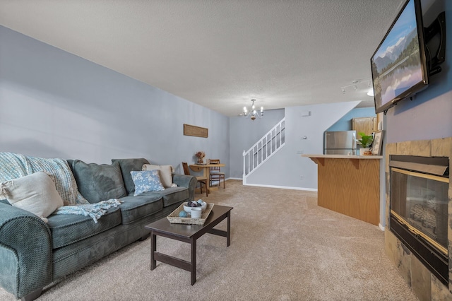 living room featuring light carpet, a textured ceiling, a chandelier, and a tiled fireplace