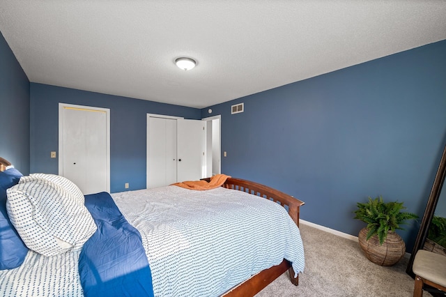 bedroom with multiple closets, light carpet, and a textured ceiling