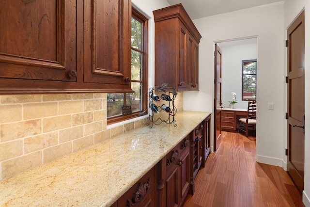 kitchen with light stone counters, a wealth of natural light, light hardwood / wood-style floors, and tasteful backsplash