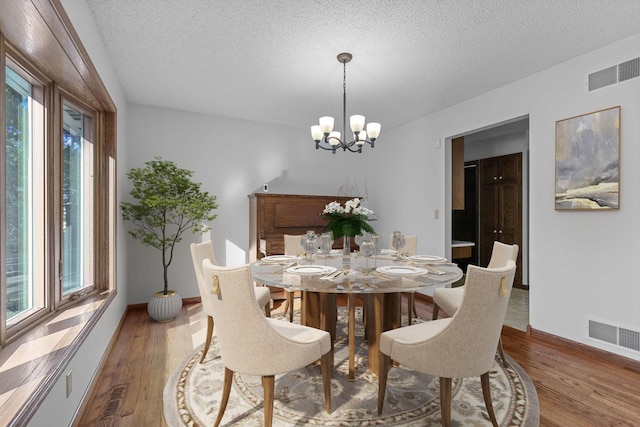 dining space with hardwood / wood-style floors, a textured ceiling, and an inviting chandelier