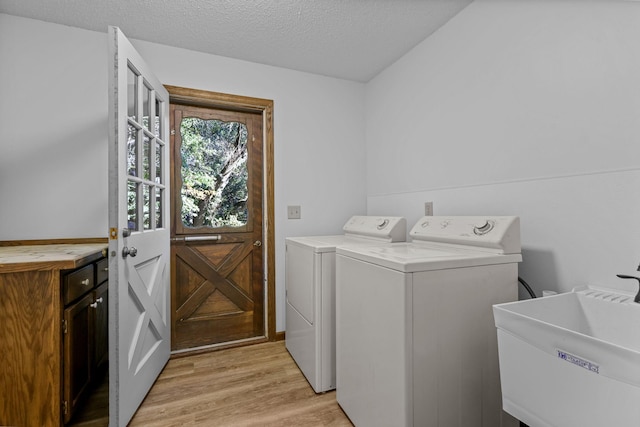 laundry room with sink, light hardwood / wood-style flooring, washing machine and dryer, and a textured ceiling