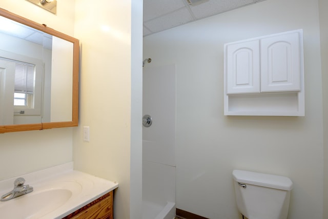 bathroom featuring walk in shower, a drop ceiling, vanity, and toilet