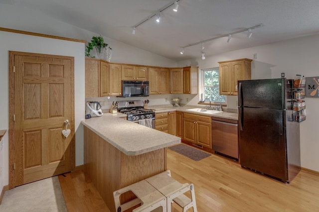 kitchen with kitchen peninsula, light wood-type flooring, vaulted ceiling, sink, and black appliances