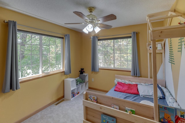 bedroom with multiple windows, ceiling fan, light colored carpet, and a textured ceiling