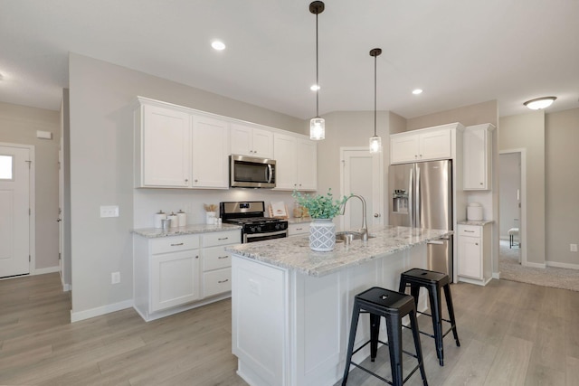 kitchen with white cabinets, sink, a center island with sink, stainless steel appliances, and light stone countertops