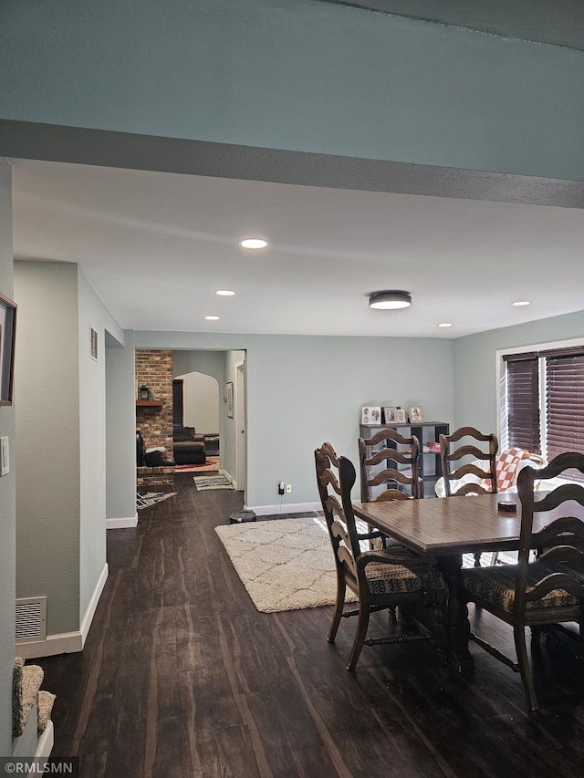 dining room featuring a brick fireplace and dark wood-type flooring