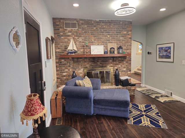 living room with a brick fireplace, brick wall, and dark hardwood / wood-style flooring