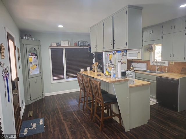 kitchen with white appliances, a kitchen island, a breakfast bar area, dark hardwood / wood-style floors, and sink