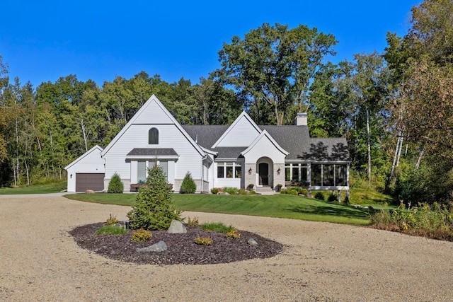 view of front of house featuring a garage, a sunroom, driveway, a chimney, and a front yard