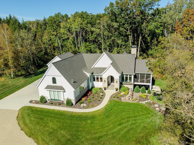 view of front of home featuring a front yard, a sunroom, and a forest view