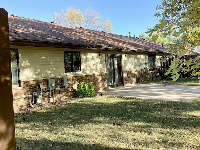 rear view of house featuring a lawn, roof with shingles, a patio, and brick siding