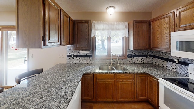 kitchen with sink, white appliances, a textured ceiling, backsplash, and dark stone countertops