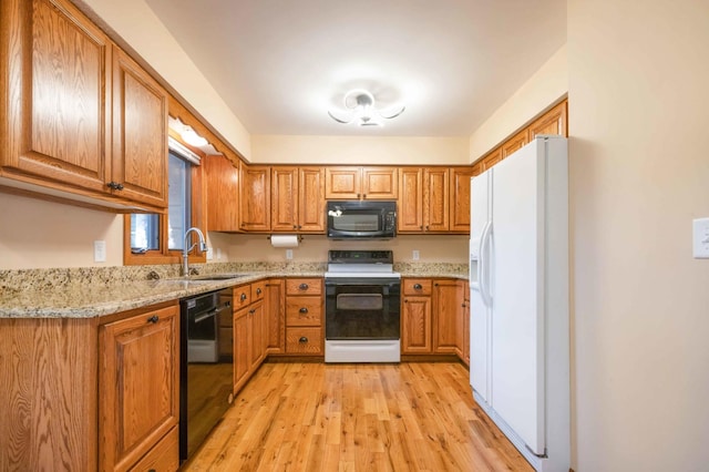 kitchen featuring light stone countertops, light hardwood / wood-style floors, sink, and black appliances