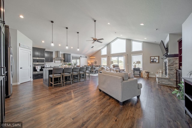 living room with high vaulted ceiling, ceiling fan, dark wood-type flooring, and a stone fireplace