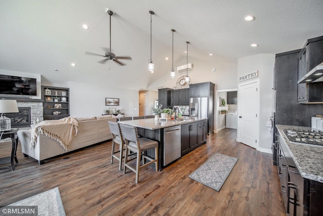 kitchen with light stone counters, an island with sink, appliances with stainless steel finishes, and high vaulted ceiling